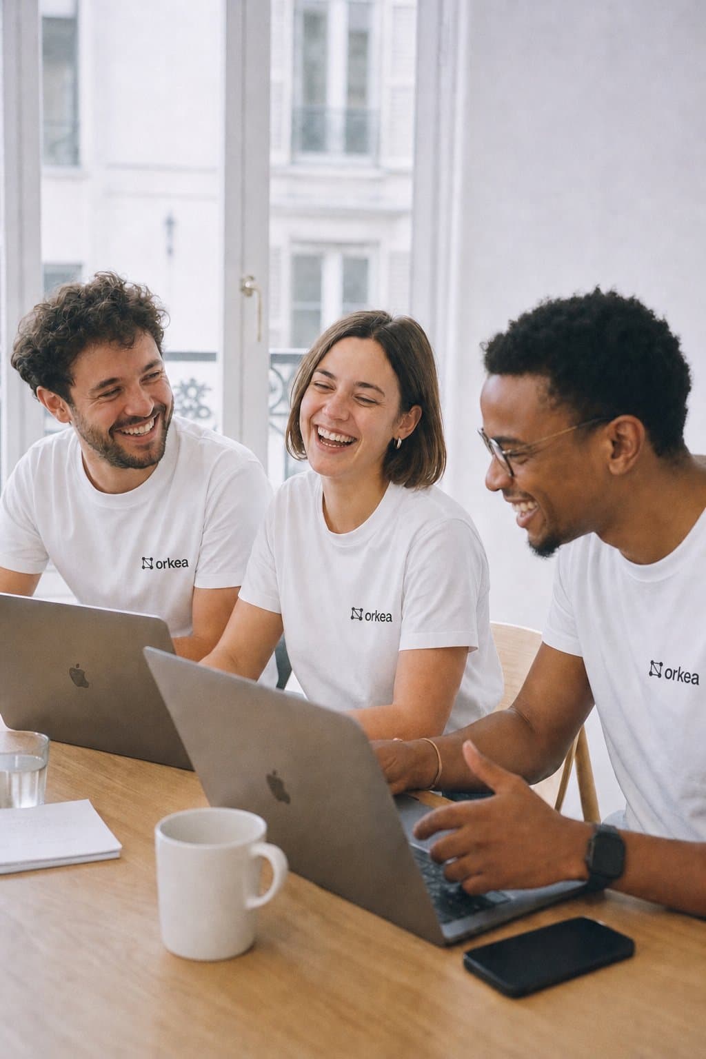 Three Centralys developers laughing together around their laptops, wearing Orkea t-shirts